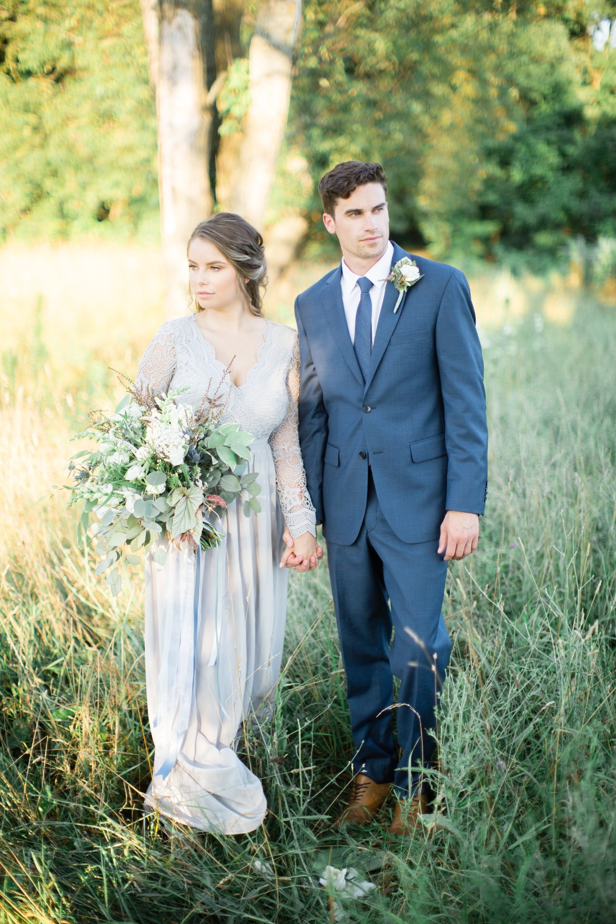 Elegant bride and groom holding hands in field on their wedding day