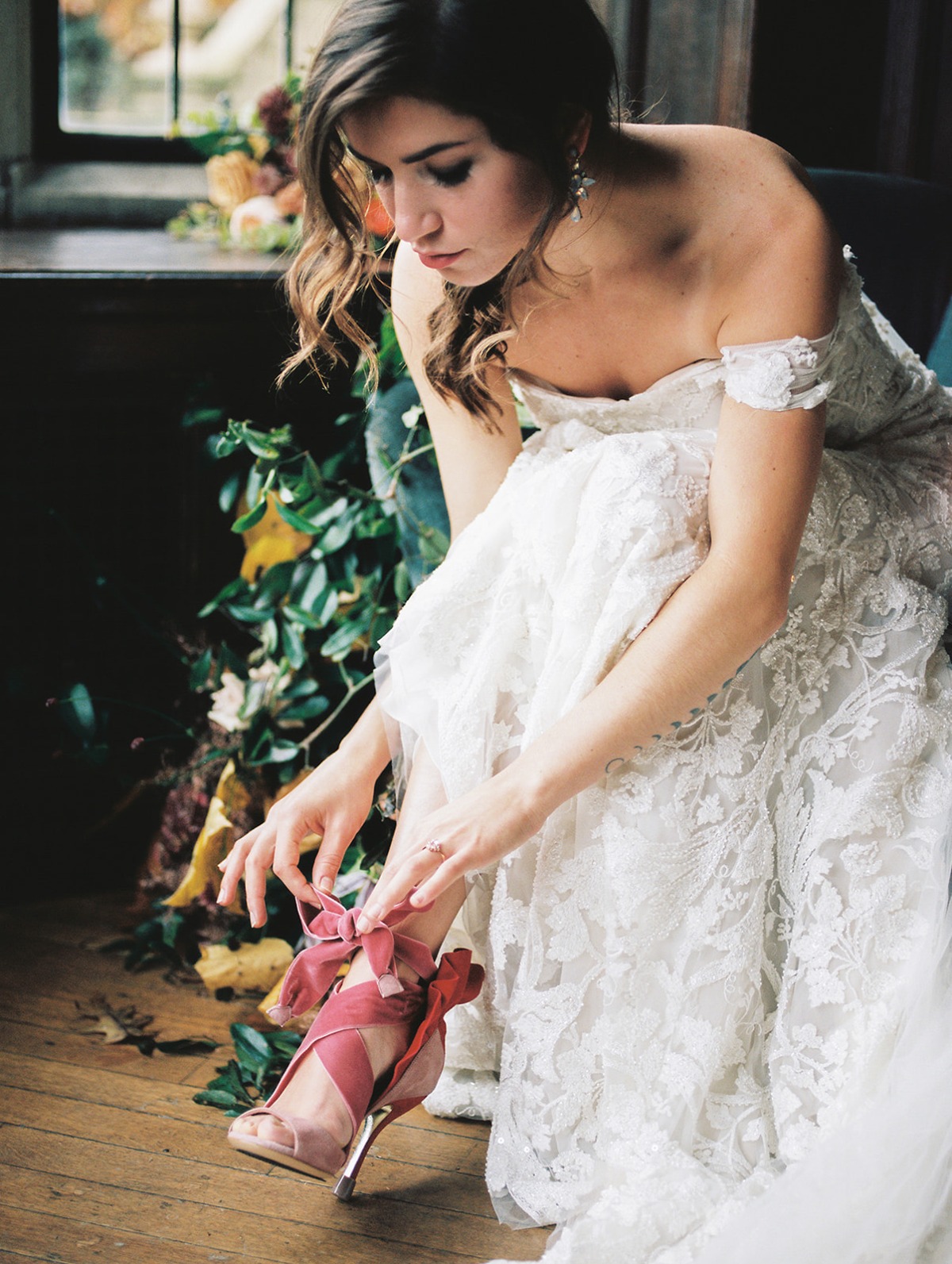 Bride in a lace gown ties the ribbon of her pink wedding shoe