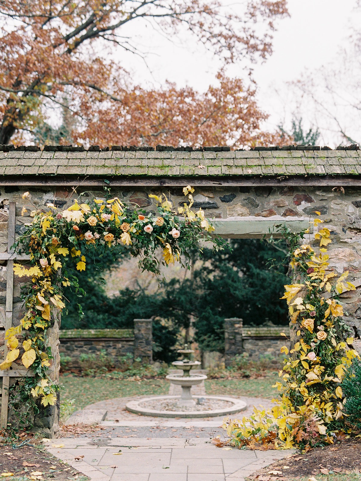 Stone archway decorated with flowers in autumn garden with fountain