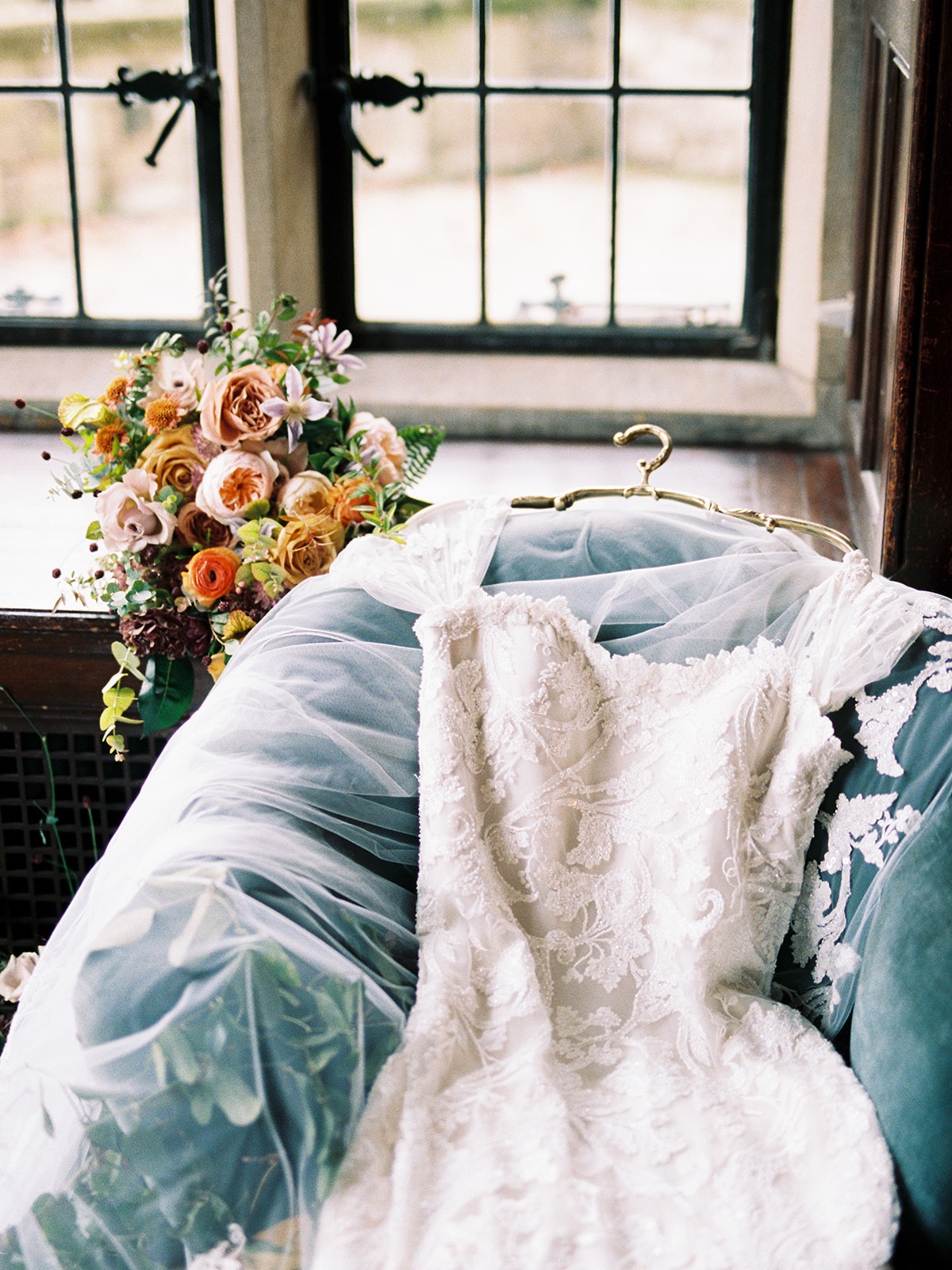 Lace wedding dress veil and bouquet on velvet couch
