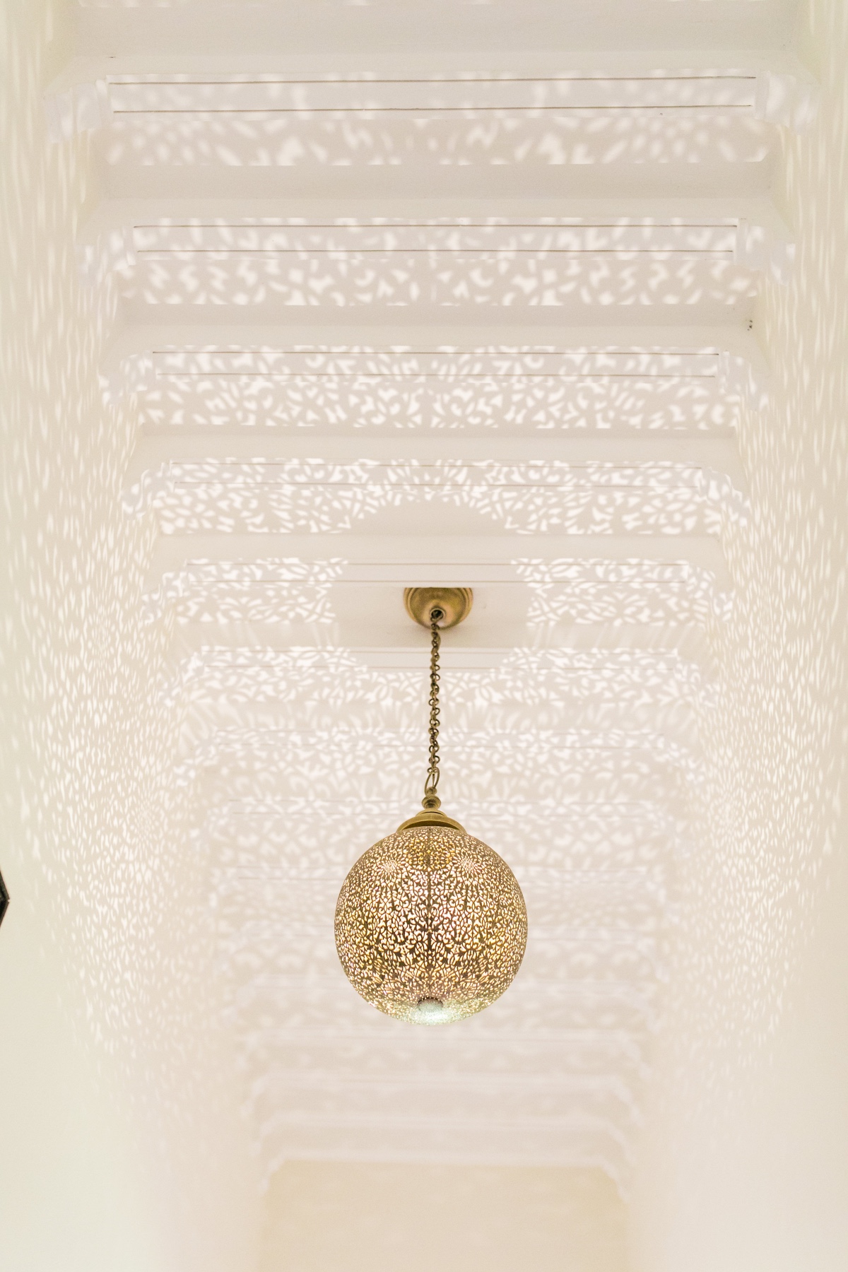 Ornate pendant lamp hangs in a hallway with patterned ceiling