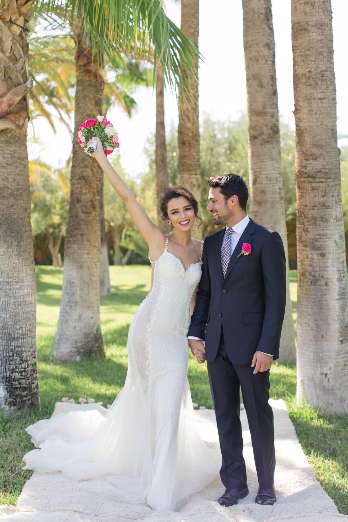 Bride raises bouquet with groom outdoors wedding portrait