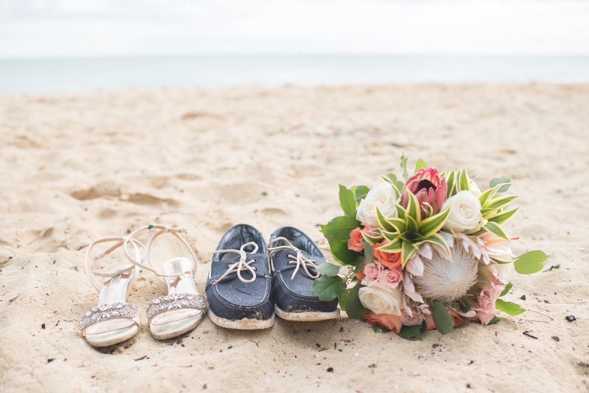 Beach wedding shoes and bridal bouquet on sandy shore