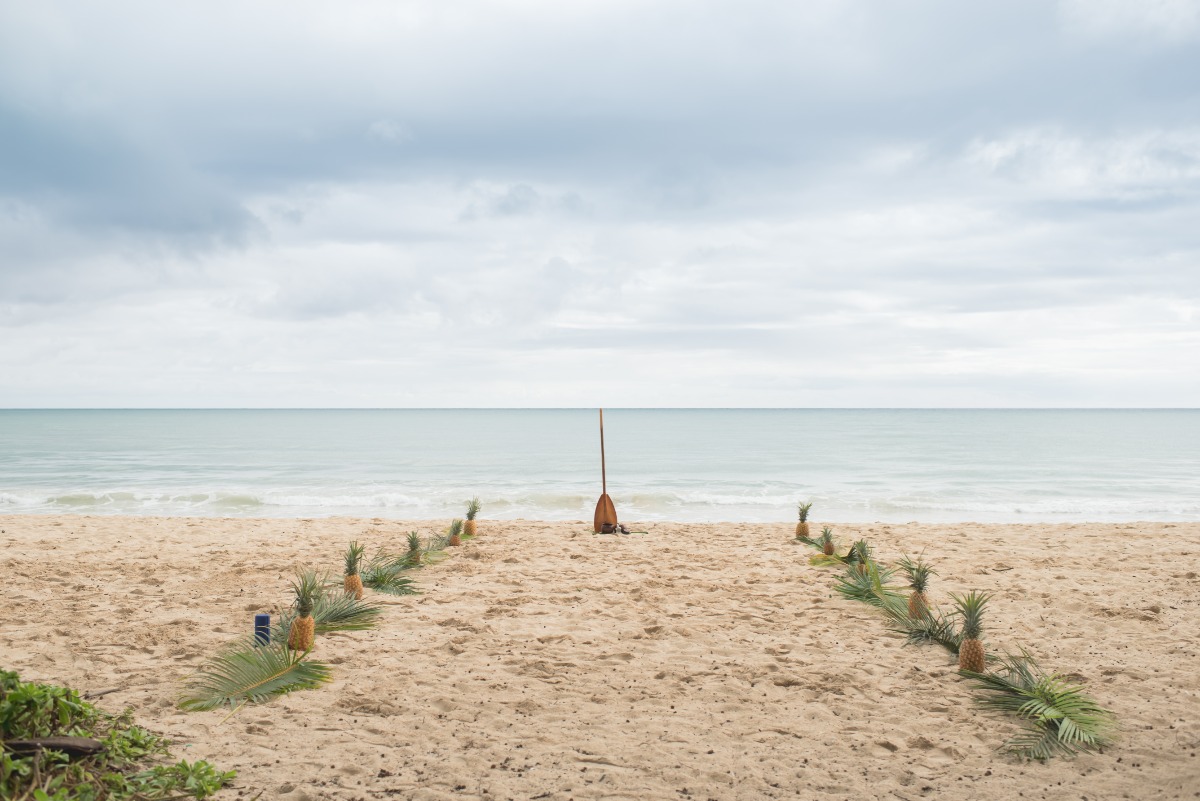 Beach ceremony setup with pineapples and paddle on a cloudy day