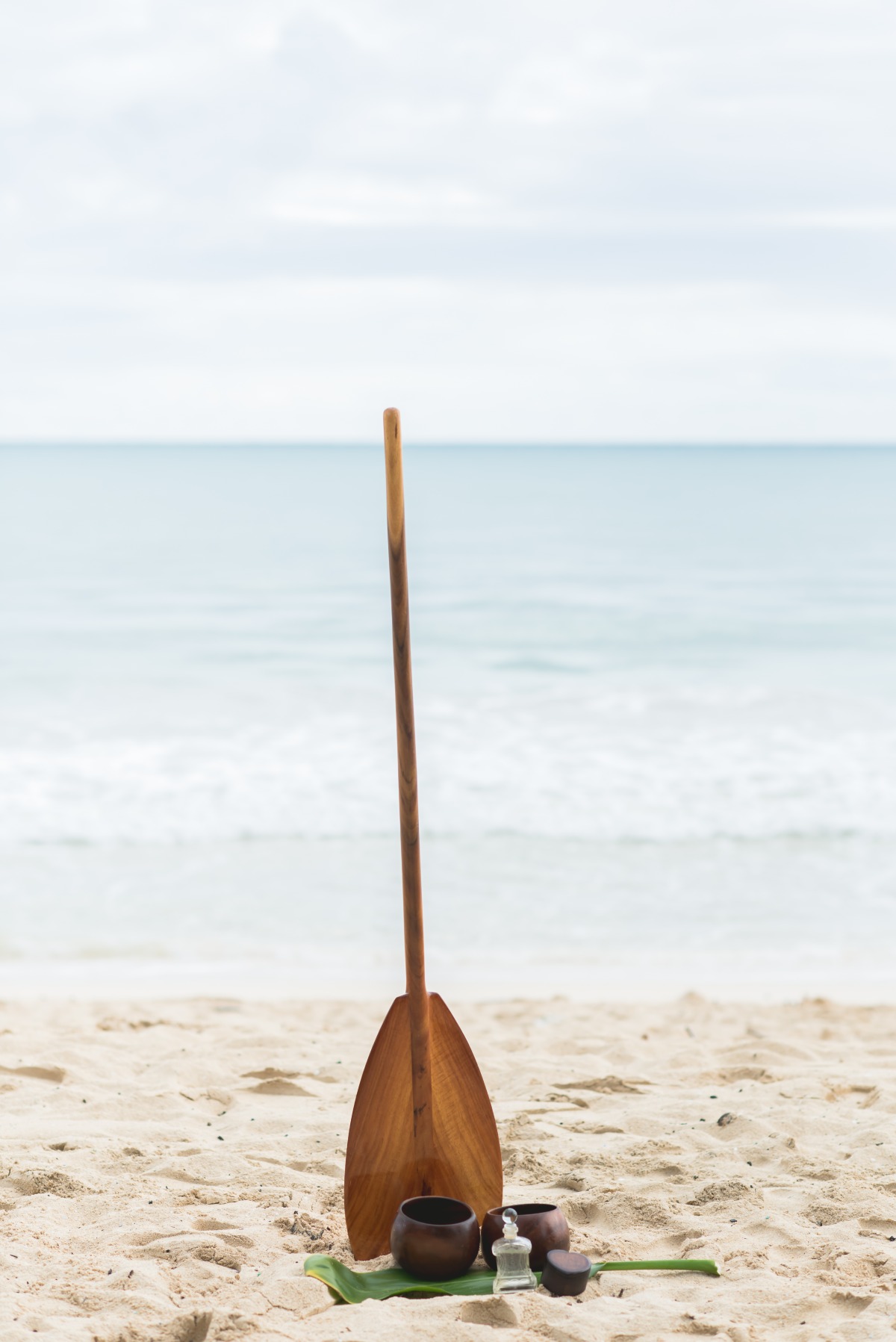 Wooden paddle and bowls on a sandy beach with the ocean in the background