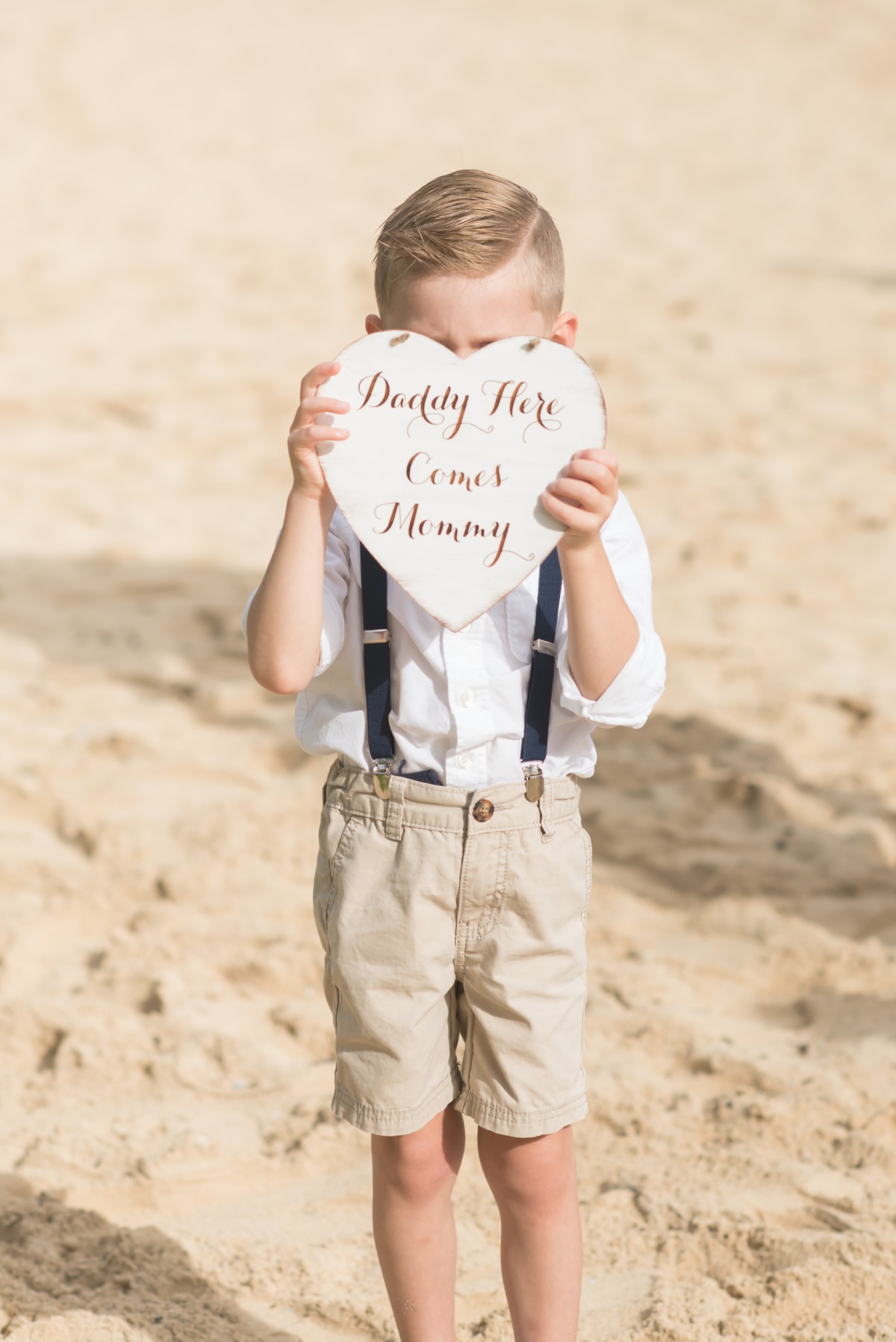 Ring bearer holding a heart sign at a beach wedding