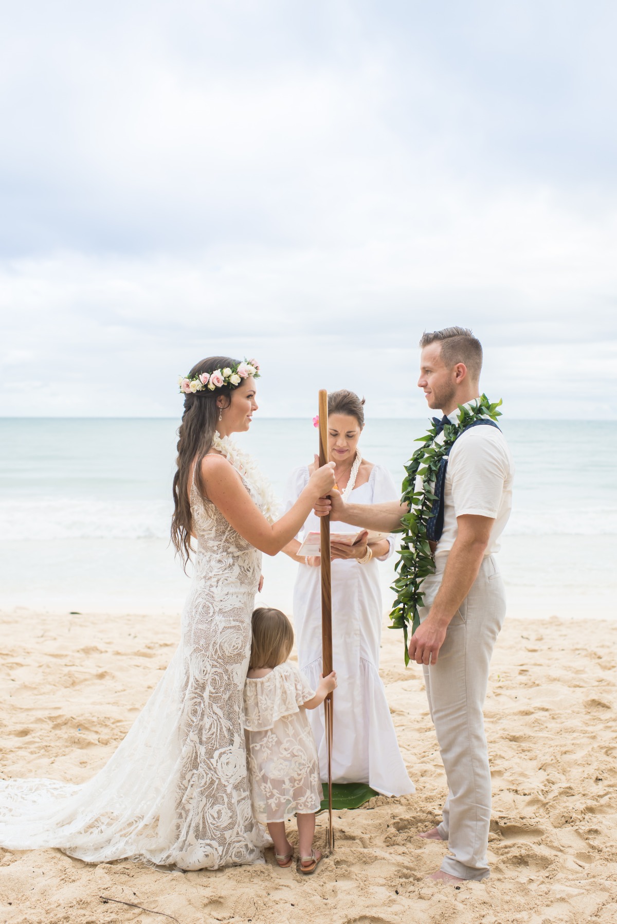 Beach wedding ceremony with bride, groom, and child on the sand