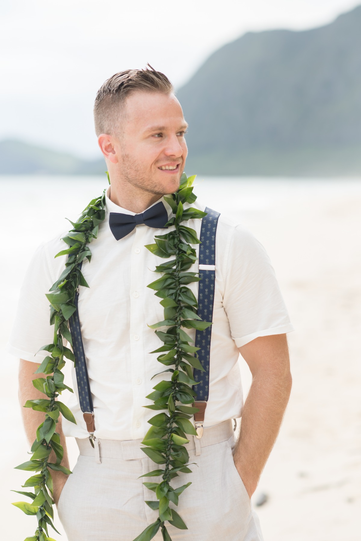 Stylish groom on the beach wearing suspenders and floral lei