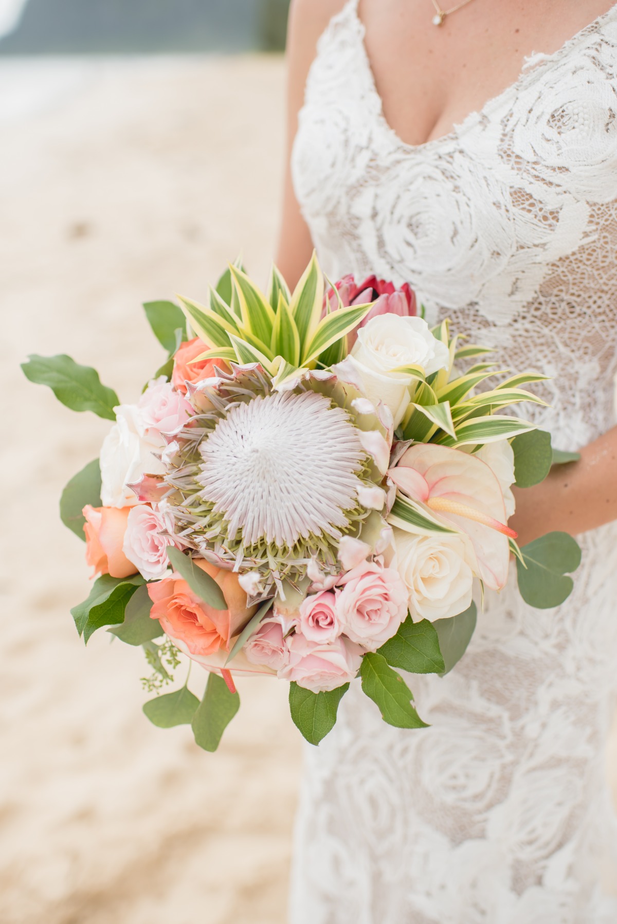 Bride in lace dress holding a colorful wedding bouquet on the beach