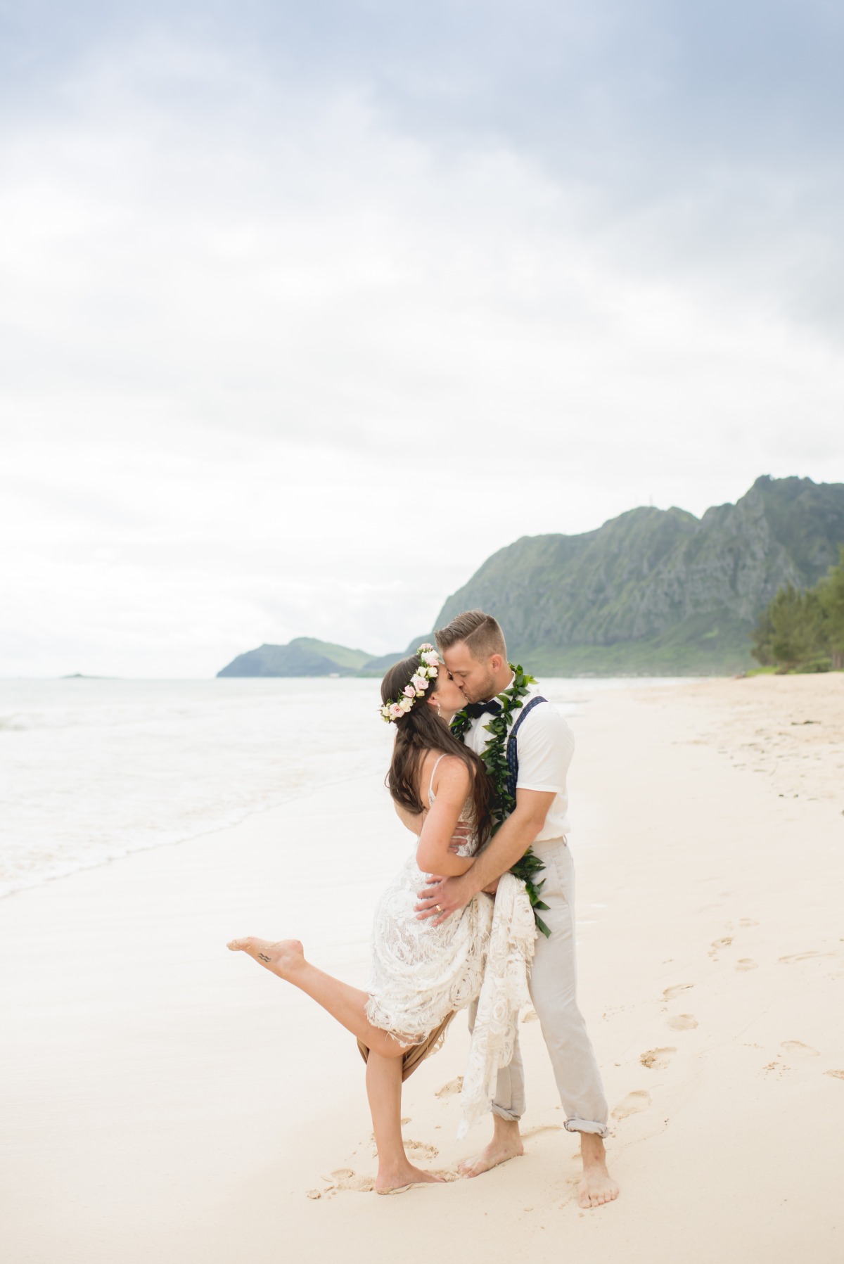 Newlyweds share a kiss on a beautiful beach with mountains in background