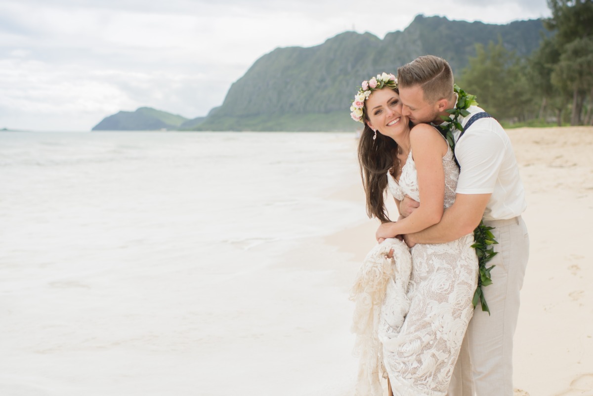Newlywed couple embraces and kisses at beach wedding ceremony