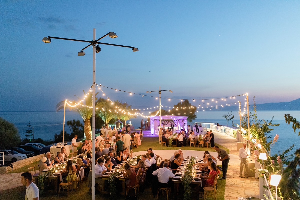 Outdoor wedding reception with string lights at dusk near ocean