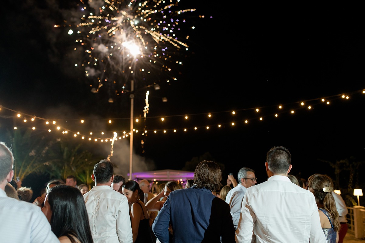 Wedding guests watch fireworks under string lights at night