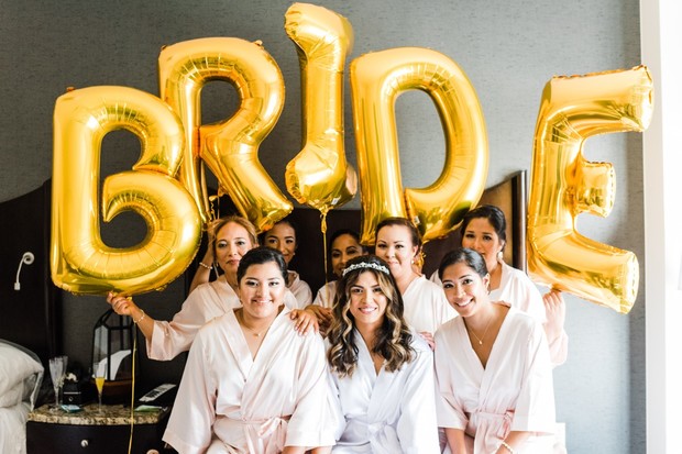 Bride and bridesmaids in robes holding gold BRIDE balloons