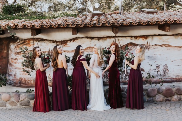 Bridesmaids in burgundy gowns pose with bride in white dress