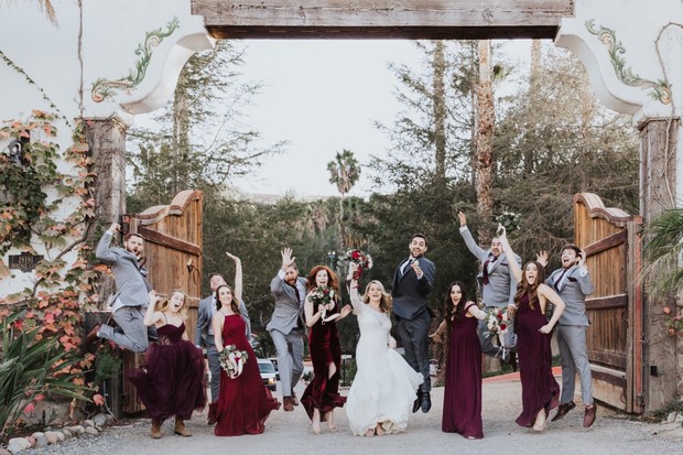Wedding party jumps joyfully under archway, celebrating the day