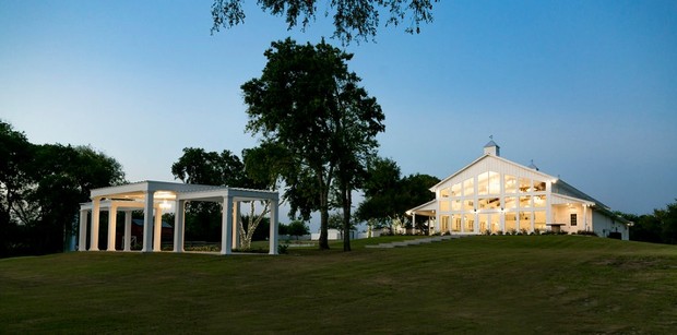A beautiful white event venue surrounded by trees on a lush green hill