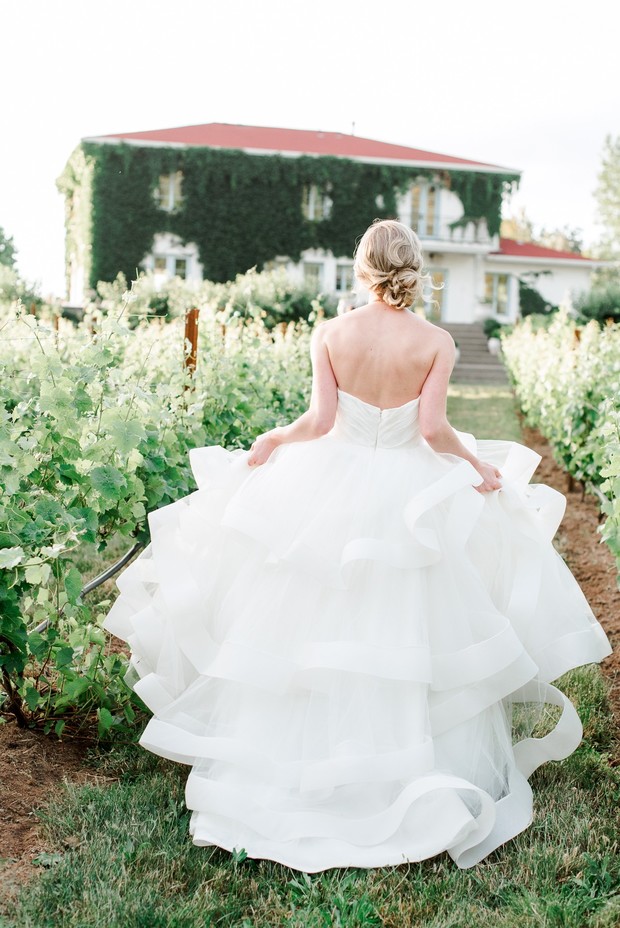 Bride in a flowing gown walks through a vineyard on her wedding day