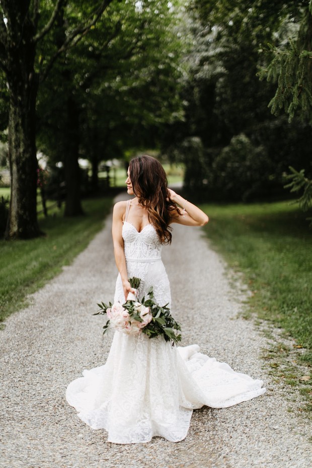 Elegant bride in lace dress holding bouquet outdoors