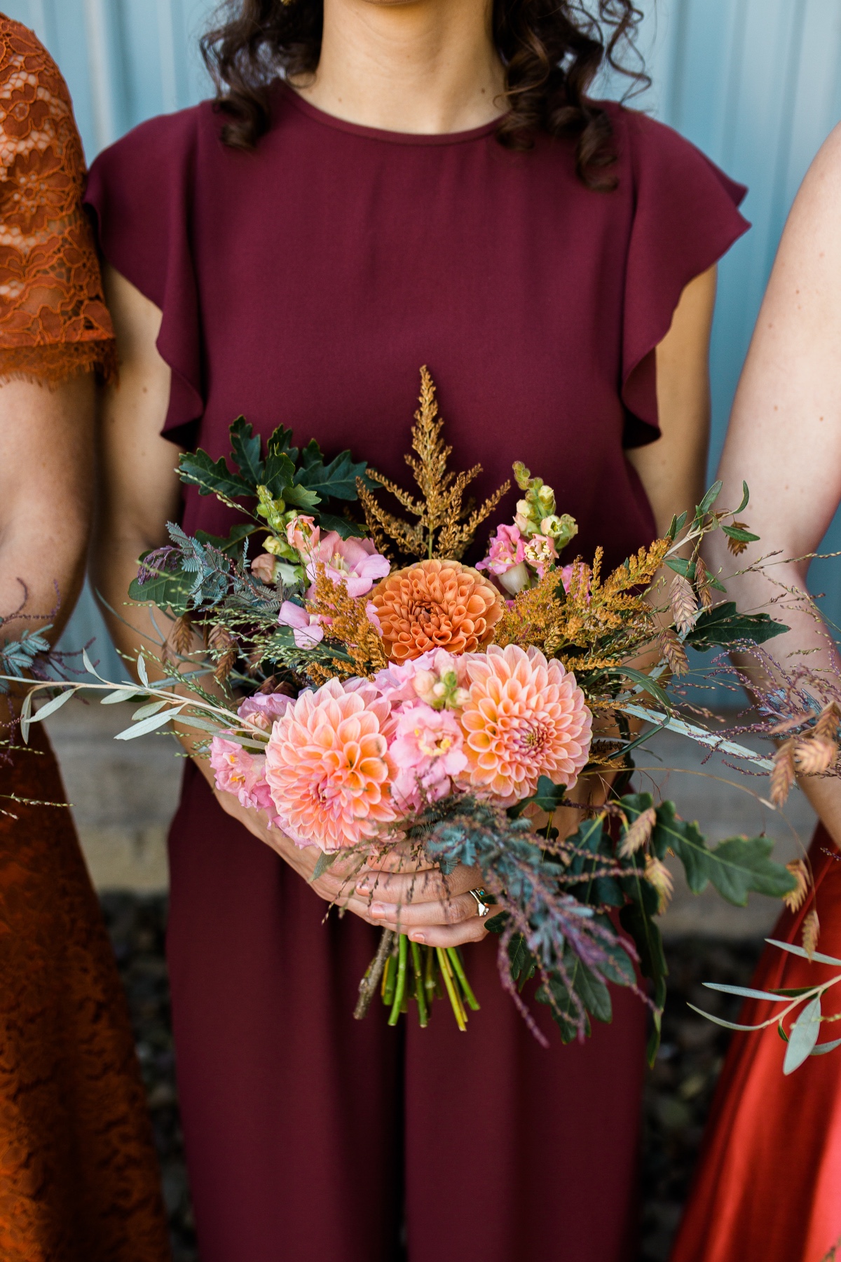 Bridesmaid in maroon holds peach dahlia wedding bouquet