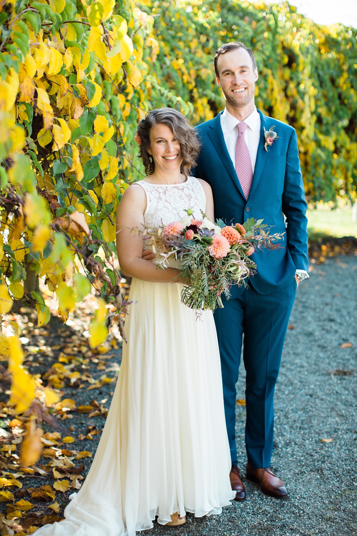 Newlyweds pose by autumn leaves with bridal bouquet