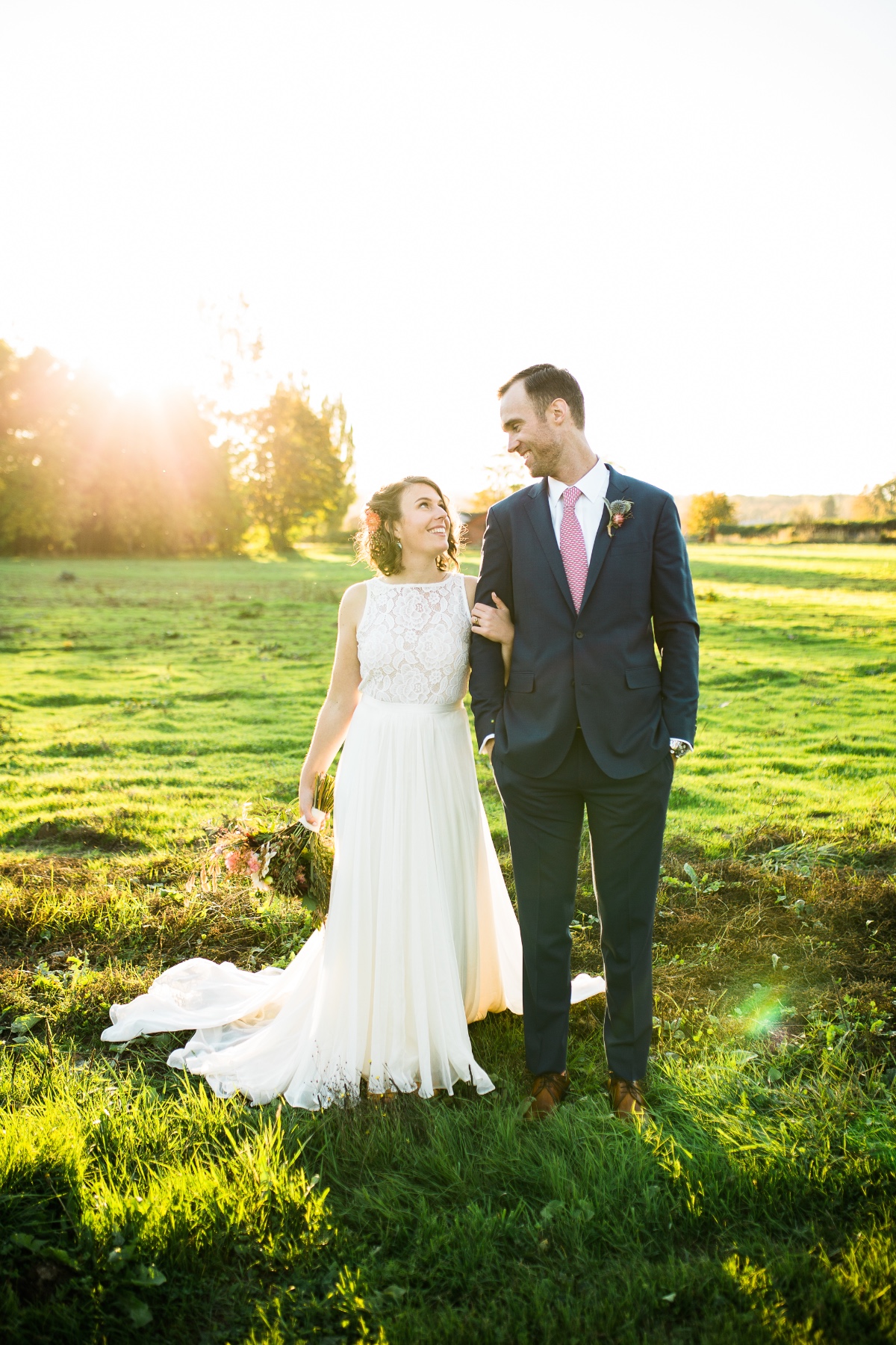 Bride and groom smile lovingly in sunny field wedding