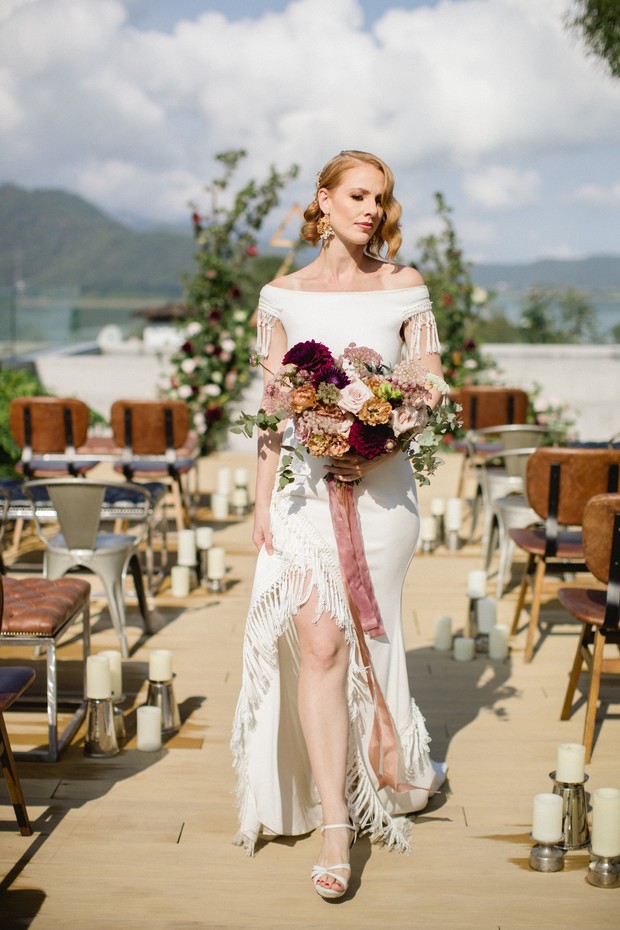 Elegant bride in fringed wedding dress holds floral bouquet