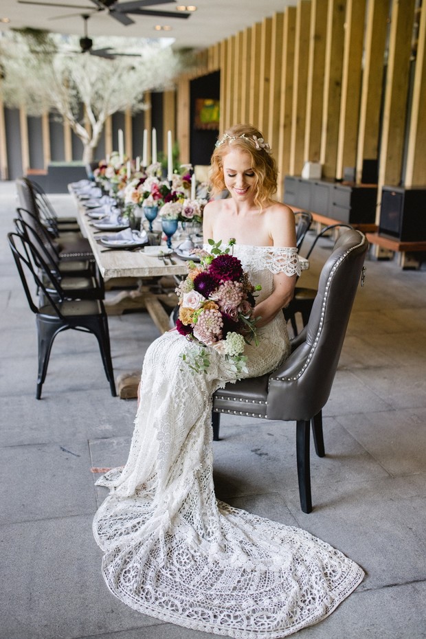 Boho bride in lace gown sits before reception table