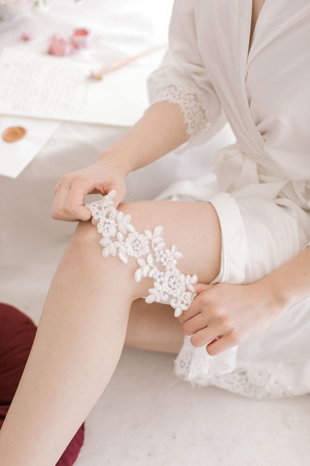 Bride in robe adjusting her delicate white lace garter