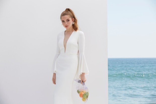 Woman in a white dress holding bag of fruit with ocean background
