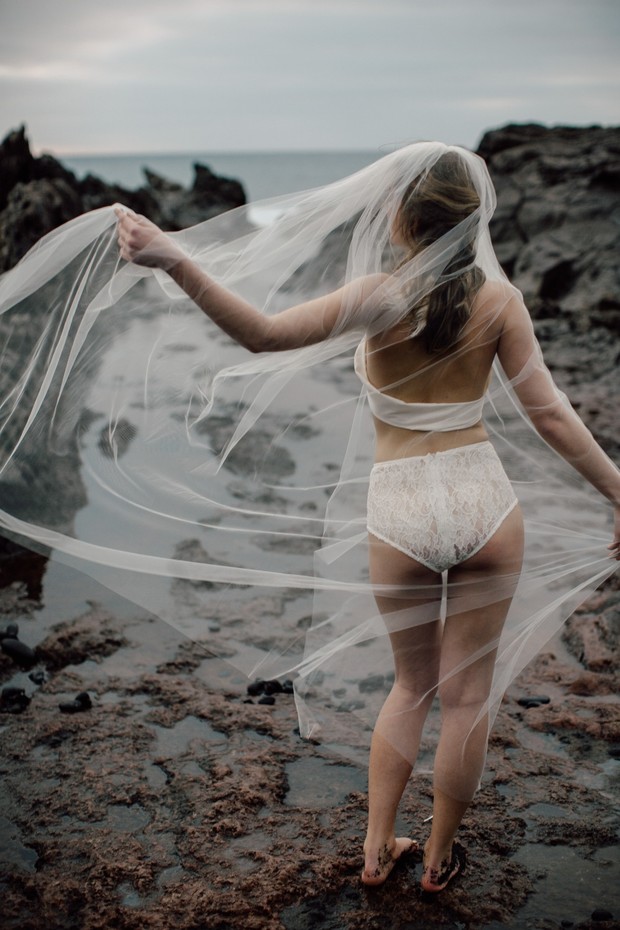 Bride in lingerie on the beach with veil flowing in the wind