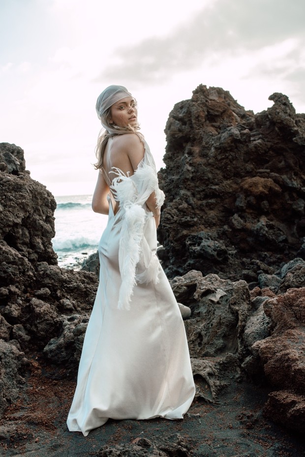 Elegant woman in white dress posing near volcanic rocks at the coast