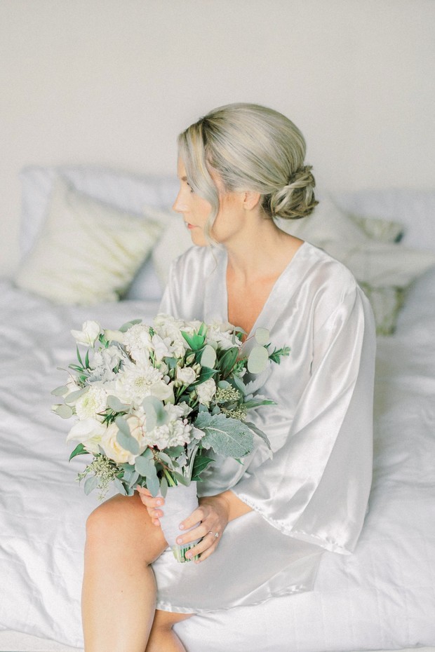 Bride in robe holding white flower wedding bouquet