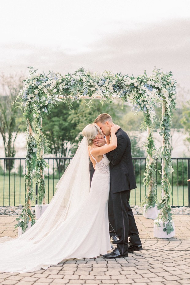 Newlyweds sharing a kiss under a floral wedding arch