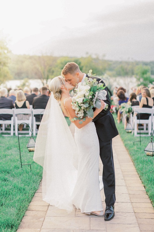 Happy newlyweds kiss on the aisle after outdoor ceremony