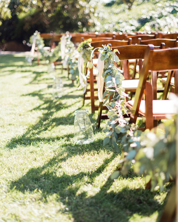 Wedding ceremony chairs decorated with greenery on a sunny day