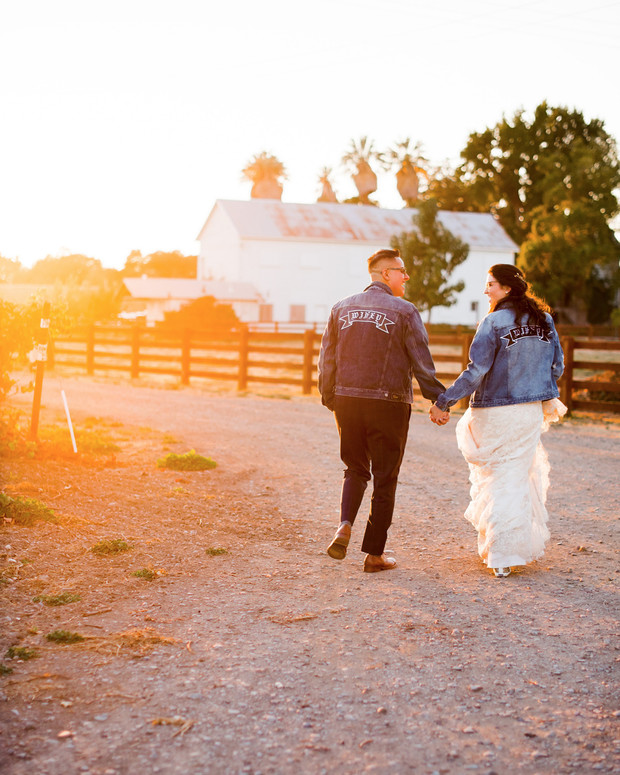 Wedding couple walking on a path with jean jackets at sunset