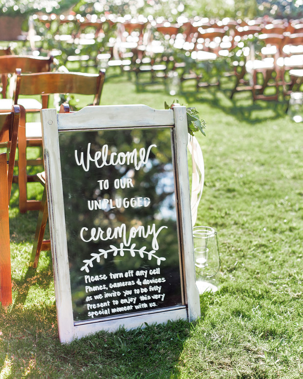 Wedding sign encouraging unplugged ceremony, green grass and chairs