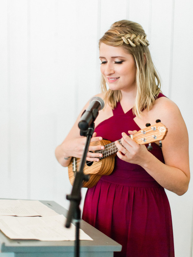Woman in burgundy dress playing ukulele, singing song