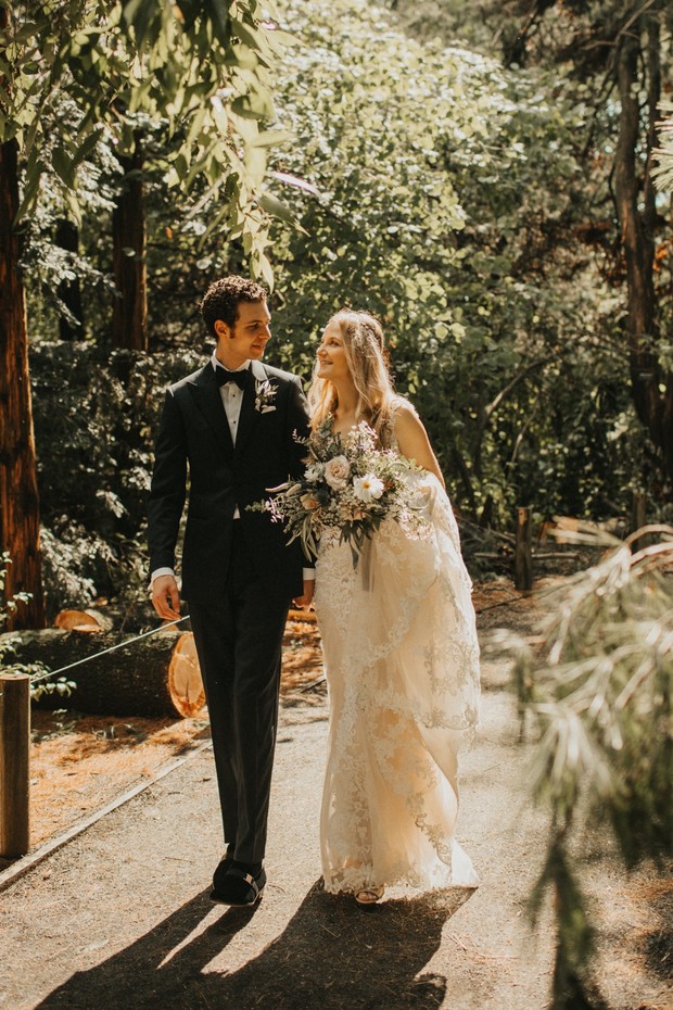 Newlyweds holding hands on a sun-dappled forest path, happy together
