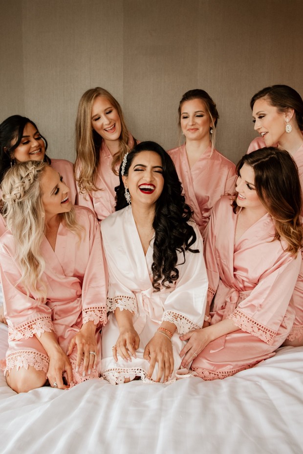 Bride surrounded by bridesmaids in matching robes, laughing