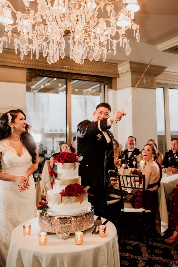 Wedding cake cut with a sword by the groom, surrounded by guests