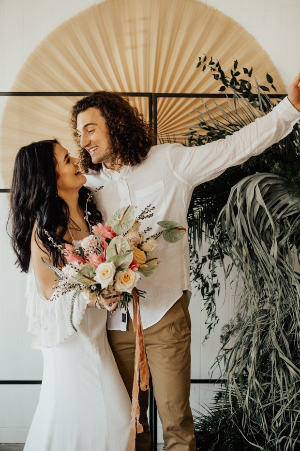 Happy boho chic wedding couple with floral bouquet
