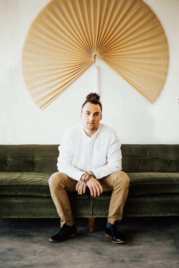 Man sits on green couch with fan decoration behind him