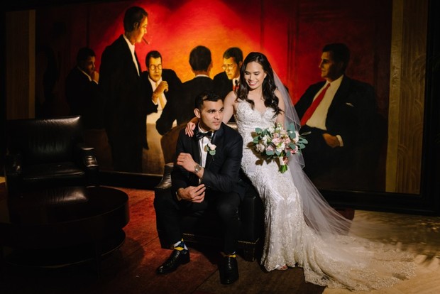 Bride and groom pose in front of a vintage mob painting