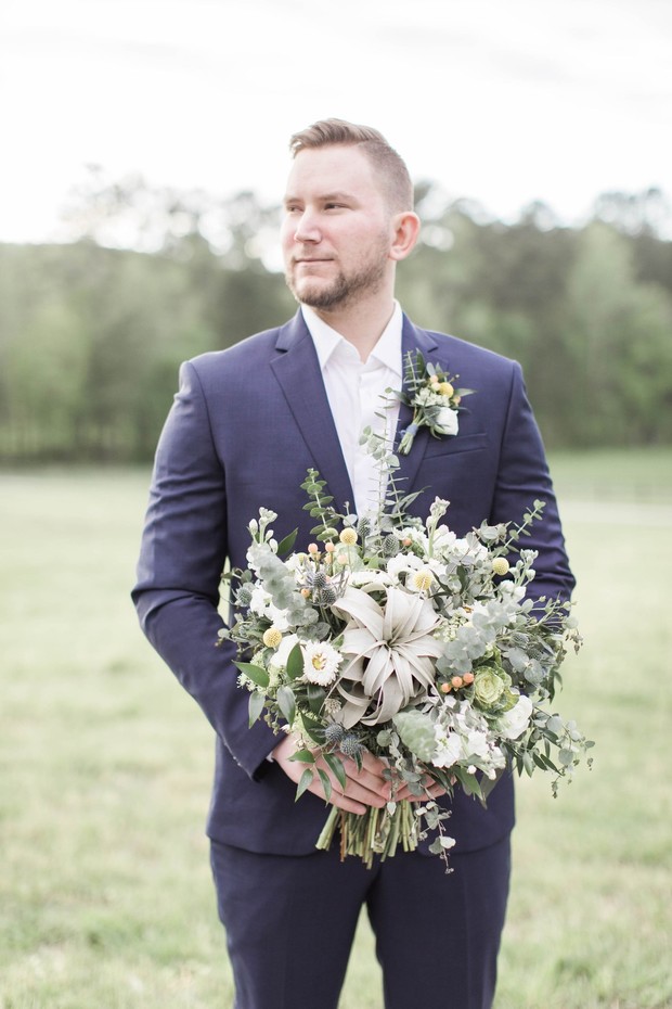 Groom in a blue suit holding a wedding bouquet outdoors