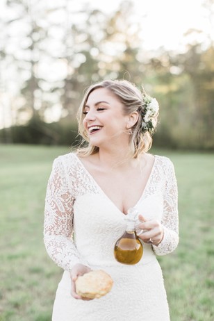 Bride in lace gown with olive oil and bread laughing