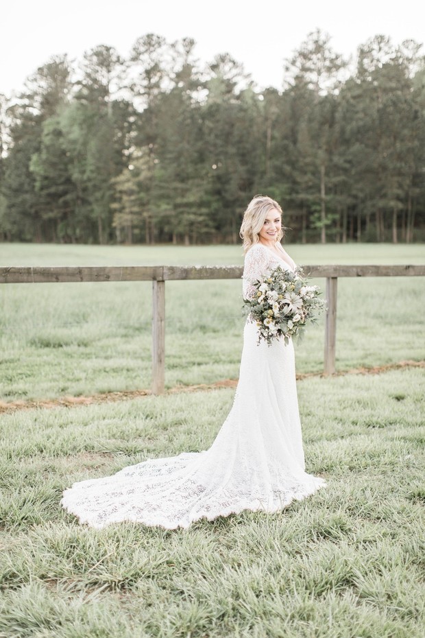 Bride in lace gown holds bouquet in rural wedding setting