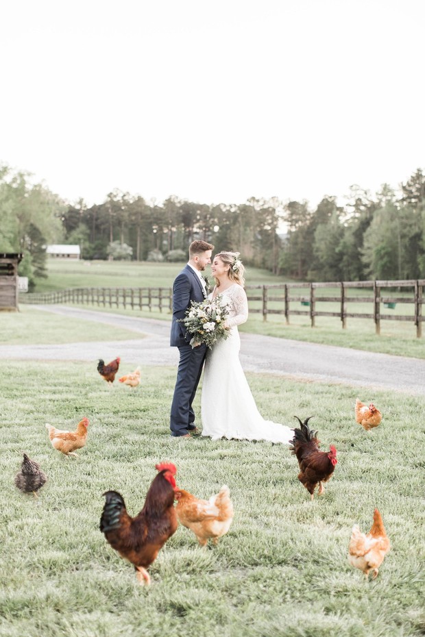 Bride and groom surrounded by chickens at farm wedding