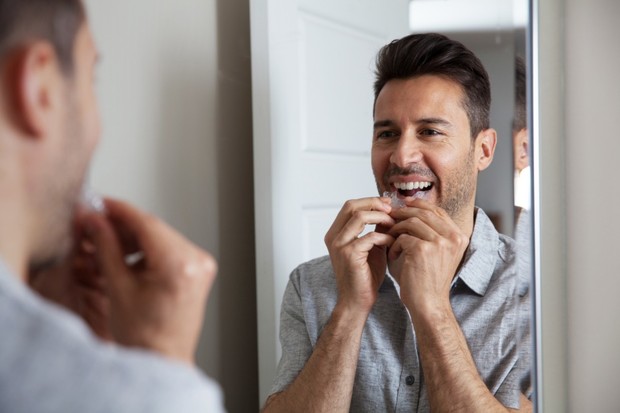 Smiling man puts on teeth aligners in front of a mirror